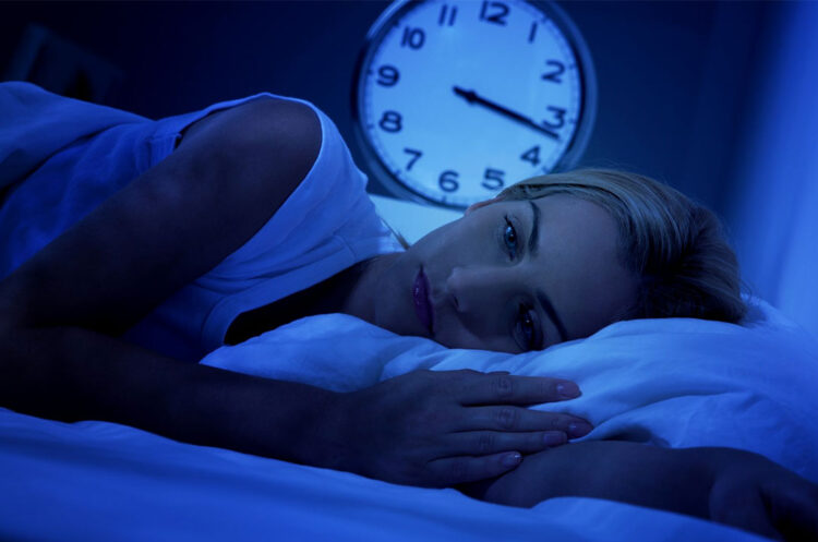 a woman lying in bed with a clock in the background