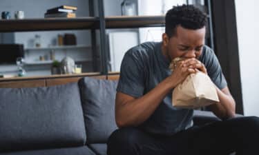 a man sitting on a couch blowing his nose into a paper bag